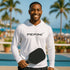 Man wearing a white hoodie with 'PEPINI' logo holding a pickleball paddle by a pool with palm trees in the background.